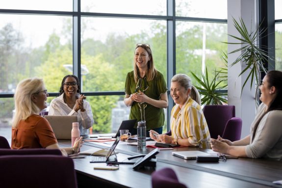 A wide-angle view of a group of women laughing and enjoying listening to each other's ideas in a business meeting in their place of work in Hexham in the NorthEast of England.