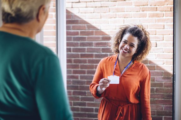 Healthcare worker showing her badge at the front door of a senior womans home.